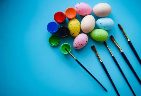 Pastel Easter Eggs Painting with Brushes on Blue Background Stock Photos
