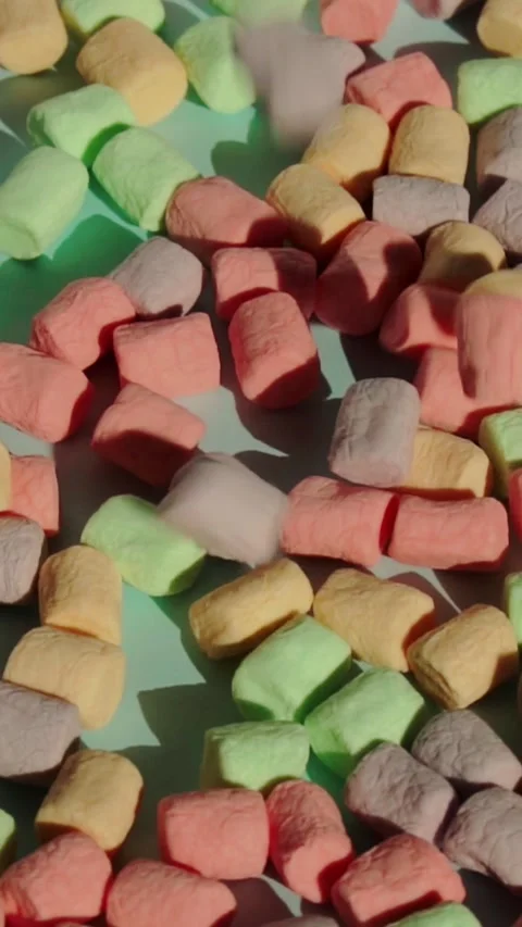 Pastel miniature marshmallows continuously drop and accumulate on flat blue Stock Footage 347272128