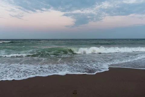 Pastel ocean waves breaking on sandy beach at sunset Stock Photos