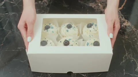 The pastry chef closes gift box with delicious cupcakes lying on the table Stockbeeldmateriaal 194449534