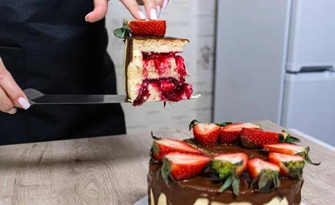The pastry chef cuts a sponge cake with cheese cream and strawberries Stock Photos