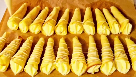 Pastry chef decorating cream filled cones with white chocolate drizzle on paper Stock Footage 326633448