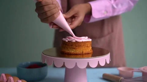 Pastry chef decorating a small sponge cake with pink cream Stock Footage 335651934