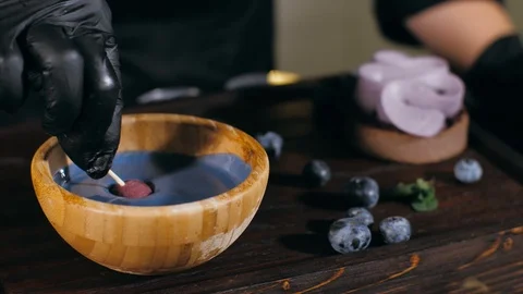 Pastry chef is dips a candy in caramel for topping a blueberry cake, close-up Stock Footage 124893005