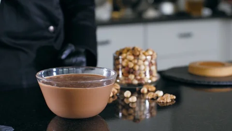 Pastry chef is dips a candy in liquid chocolate with nuts for making a cake Stock Footage 124900673
