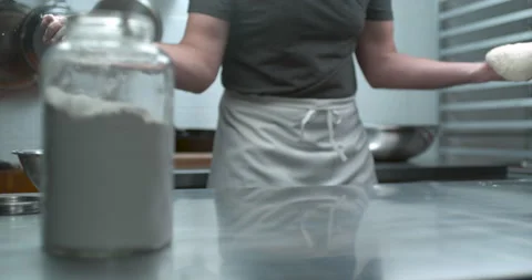 Pastry chef drops flour while holding dough dough over a metal kitchen work coun Stock Footage 199455747
