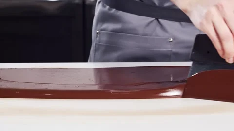 Pastry chef in grey uniform tempering melted chocolate on a white stone table Video stock 156361734