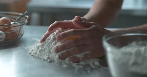 Pastry chef mixes a raw egg with flour on a metal counter top next to a metal ba Video stock 199463687