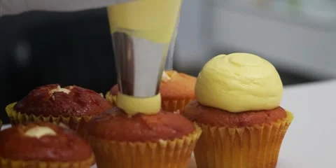 Pastry Chef Piping Smooth Yellow Frosting on Freshly Baked Cupcake - Close Up Stock Footage 343588832