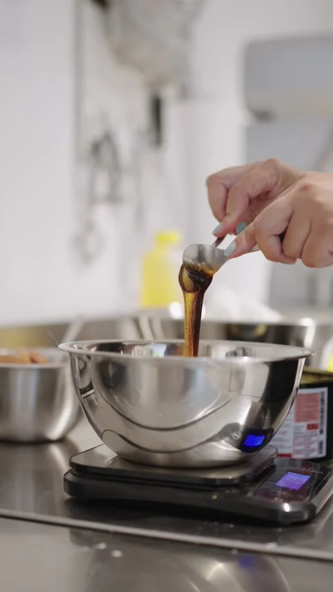 Pastry chef pouring date molasses into stainless steel bowl on digital kitchen Stock Footage 314002480