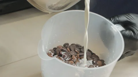 A pastry chef pours hot milk into a container with chocolate tablets for making Stock Footage 144042071