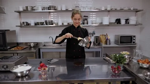 A pastry chef pours melted chocolate from a bowl onto a metal table in a kitchen Stock Footage 136834599