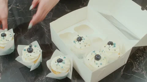 The pastry chef puts the cupcakes into the present box on the table Stockbeeldmateriaal 194449360