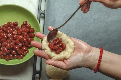 Pastry chef puts a spoonful of cherry in prepared bread dough Photos