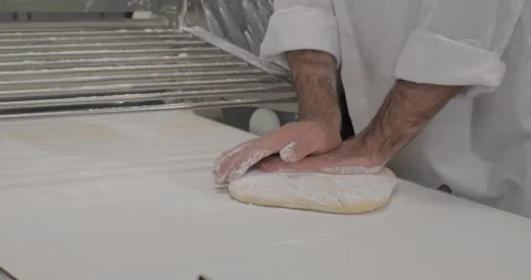 Pastry chef rolling dough on a dough sheeter rolling machine in a bakery kitchen Stock Footage 293822778