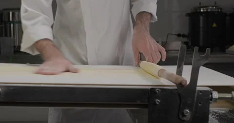 Pastry chef rolling thin dough on a rolling pin, using dough sheeter rolling Stock Footage 293826081
