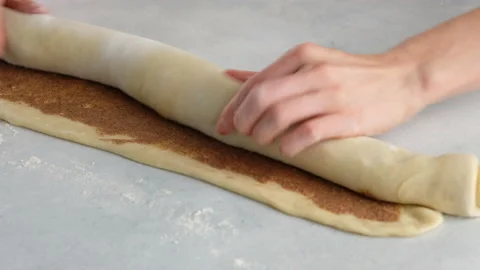 Pastry chef rolls cinnamon dough roll for buns. Female hands preparing cinnabon Stock Footage 141369802