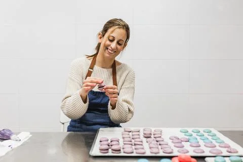 Pastry chef smiling while enjoying preparing colorful macaroons in the kitchen Stock Photos