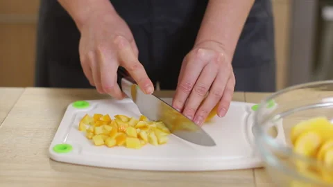 A pastry chef in a tunic and apron cuts oranges in a bright kitchen. Stock Footage 231232955