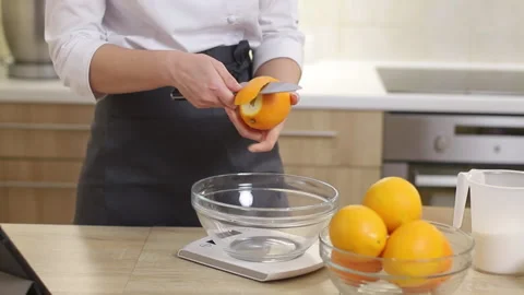 A pastry chef in a tunic and apron peels oranges in a bright kitchen. Stock Footage 231233161