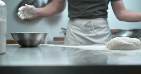 Pastry chef in white apron claps hands as flour bursts off into a cloud over a m Stock Footage 199462798