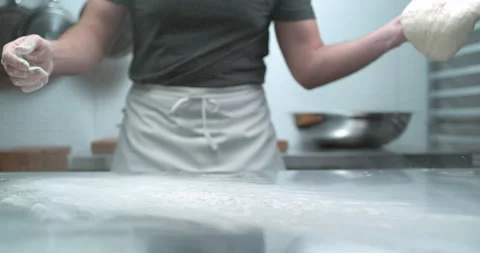 Pastry chef in white apron drops dough on a metal kitchen work counter with doug Stock Footage 199456980