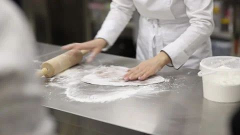 A pastry chef in a white uniform with a rolling pin rolls out the dough Stock Footage 121035403