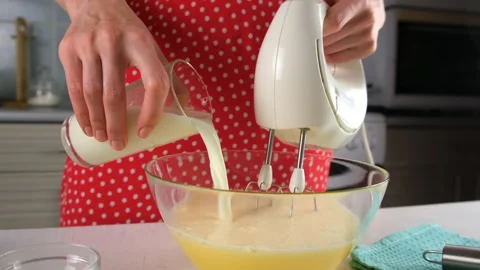 Pastry chef woman hands adding milk to batter while whisking with electric mixer Stock Footage 311527552