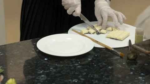 In pastry shop on the table chef with gloves cuts white chocolate. Stock Footage 85868868
