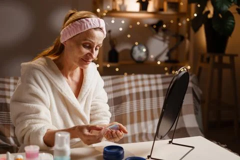 Patch Application Process. Mature woman in bathrobe before mirror applying .. 스톡 사진
