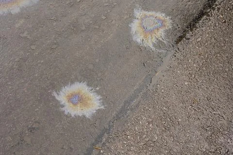 A patch of spilt oil has mixed with rain to show iridescent rainbow colours o Stock Photos