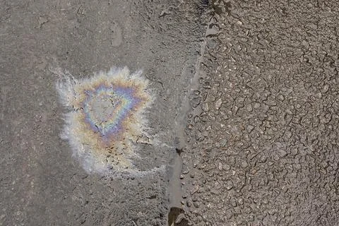 A patch of spilt oil has mixed with rain to show iridescent rainbow colours o Stock Photos