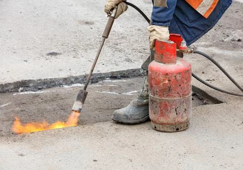 Patching a road by heating a damaged asphalt surface with a gas burner. Stock Photos