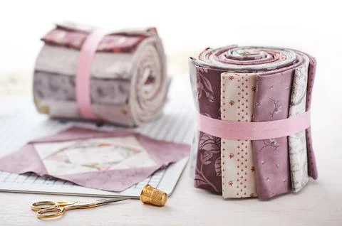 Patchwork block on craft mat, rolls of fabric, sewing accessories on white .. Fotos de archivo