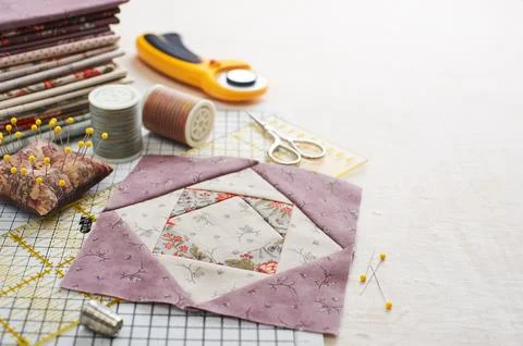 Patchwork block on craft mat, stack of fabric, sewing accessories on white .. Fotos Stock