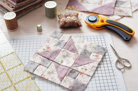 Patchwork block on craft mat, stack of fabric, sewing accessories on white .. Fotos de archivo