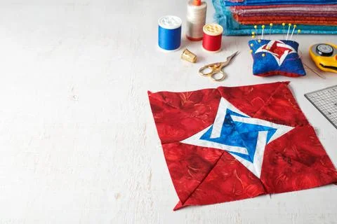 Patchwork block, pin cushion and quilting accessories on white wooden surface 스톡 사진