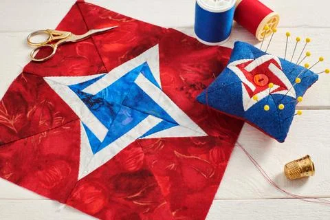 Patchwork block, pin cushion and sewing accessories on white wooden surface Fotos de archivo