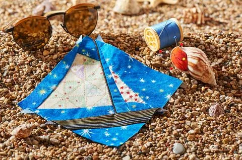 Patchwork block, spool of thread, pin cushion and sunglasses lie on sea sto.. Stock-Fotos