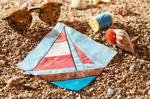 Patchwork block, spool of thread, pin cushion and sunglasses lie on sea sto.. Stock-Fotos