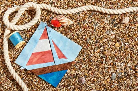 Patchwork block, spool of thread, pin cushion and rope lie on sea stones of.. Stock Photos