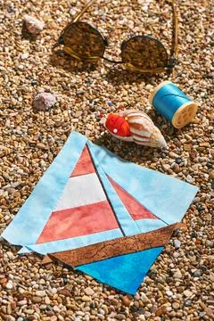 Patchwork block, spool of thread, pin cushion and sunglasses lie on sea sto.. Stock-Fotos