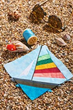 Patchwork block, spool of thread, pin cushion and sunglasses lie on sea sto.. Stock Photos