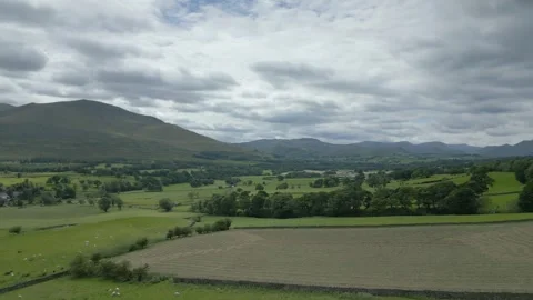 Patchwork fields countryside and mountains in distance on cloudy summer Stock Footage 247975568