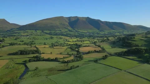 Patchwork green fields and stream with flight towards mountains on sunny Video stock 248497823