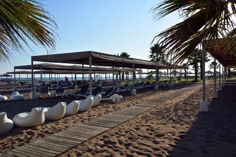 Path along the wooden decking on the beach to the sea between rows of sunbeds Stock Photos