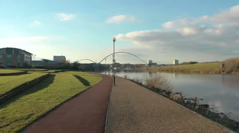 Path beside urban river leading to Infinity Bridge with zoom in Stock Footage 1059366