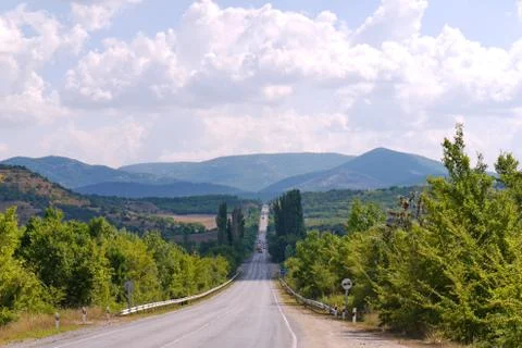 The path is between the trees and going to the mountains, under the sky with  Stock Photos