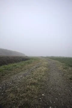 Path bordered by a ditch next to a field on a foggy day in the italian coun.. Stock Photos