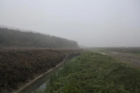 Path bordered by a ditch next to a field on a foggy day in the italian coun.. Stock Photos